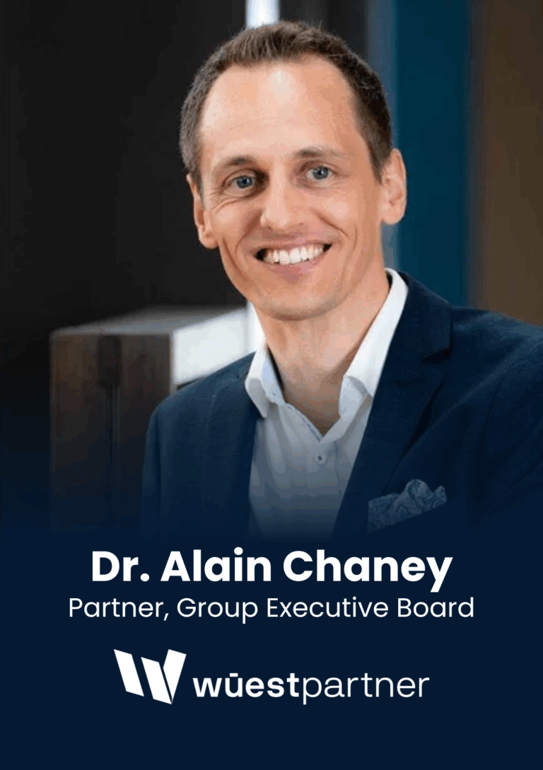 Professional head-and-shoulders portrait of a smiling man in a navy suit and white shirt, with a dark background and company logo partially visible.