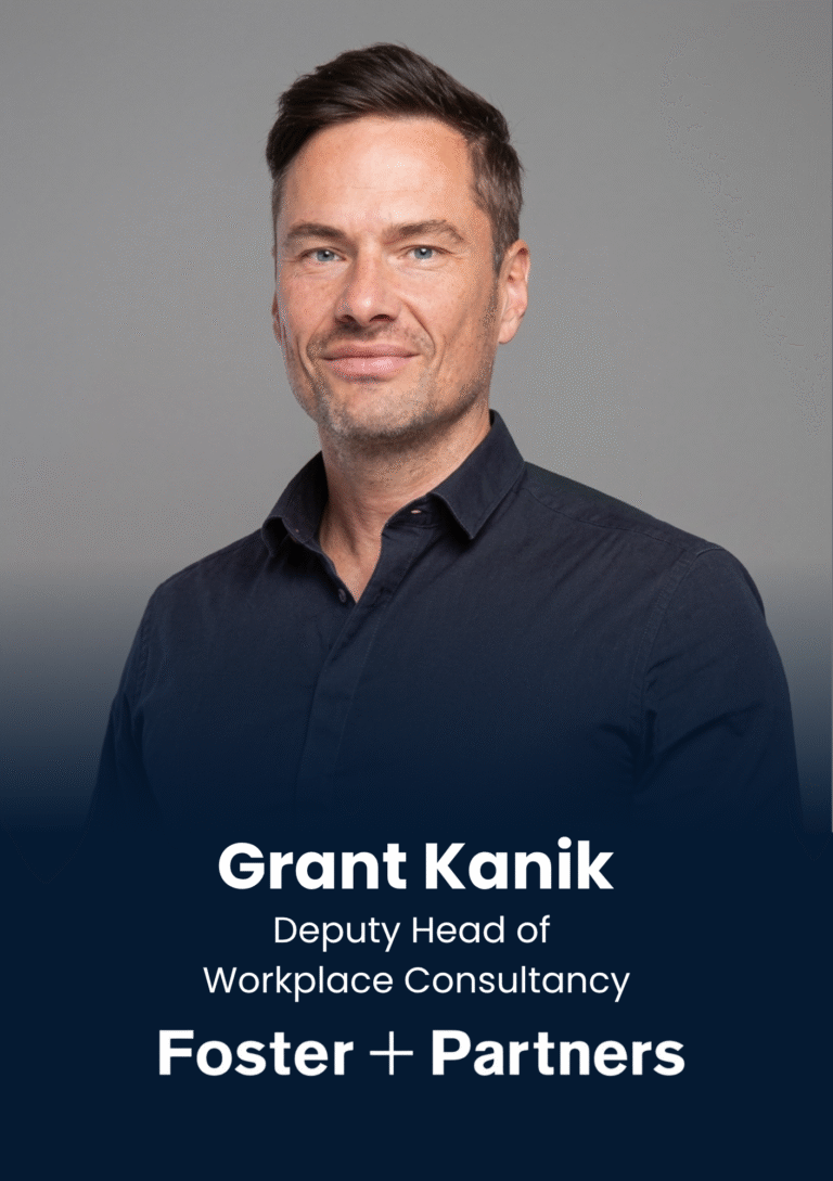 Portrait of Grant Kanik, Deputy Head of Workplace Consultancy at Foster + Partners, wearing a dark shirt against a gray backdrop, looking at the camera.