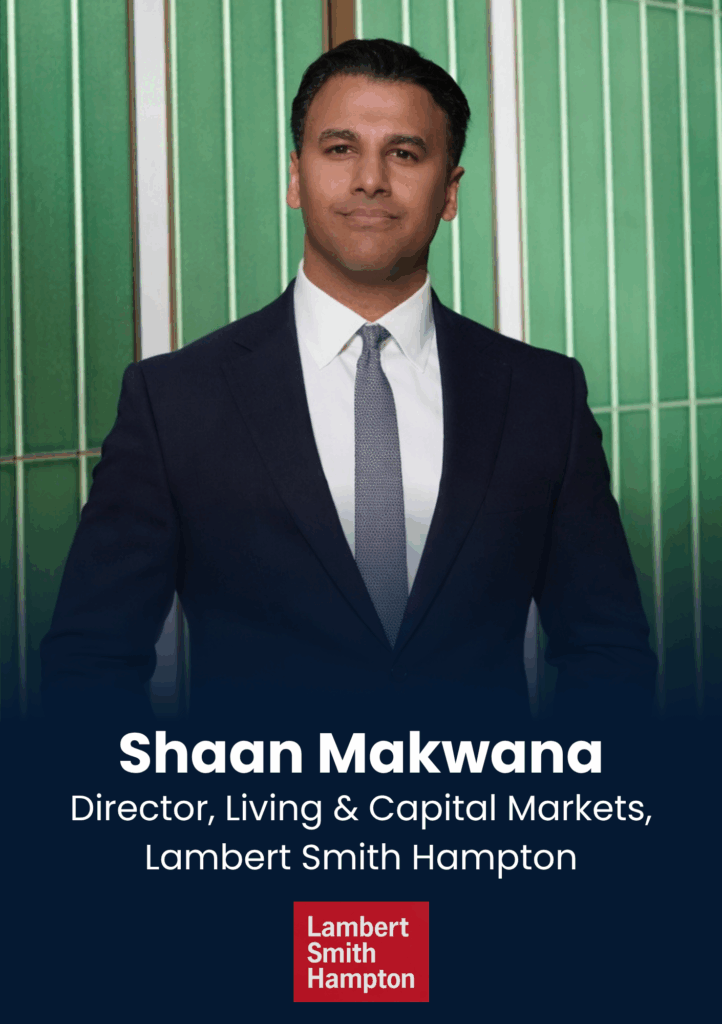 Headshot of Shaan Makwana in a dark suit and tie, standing against a green panel backdrop, looking confident.
