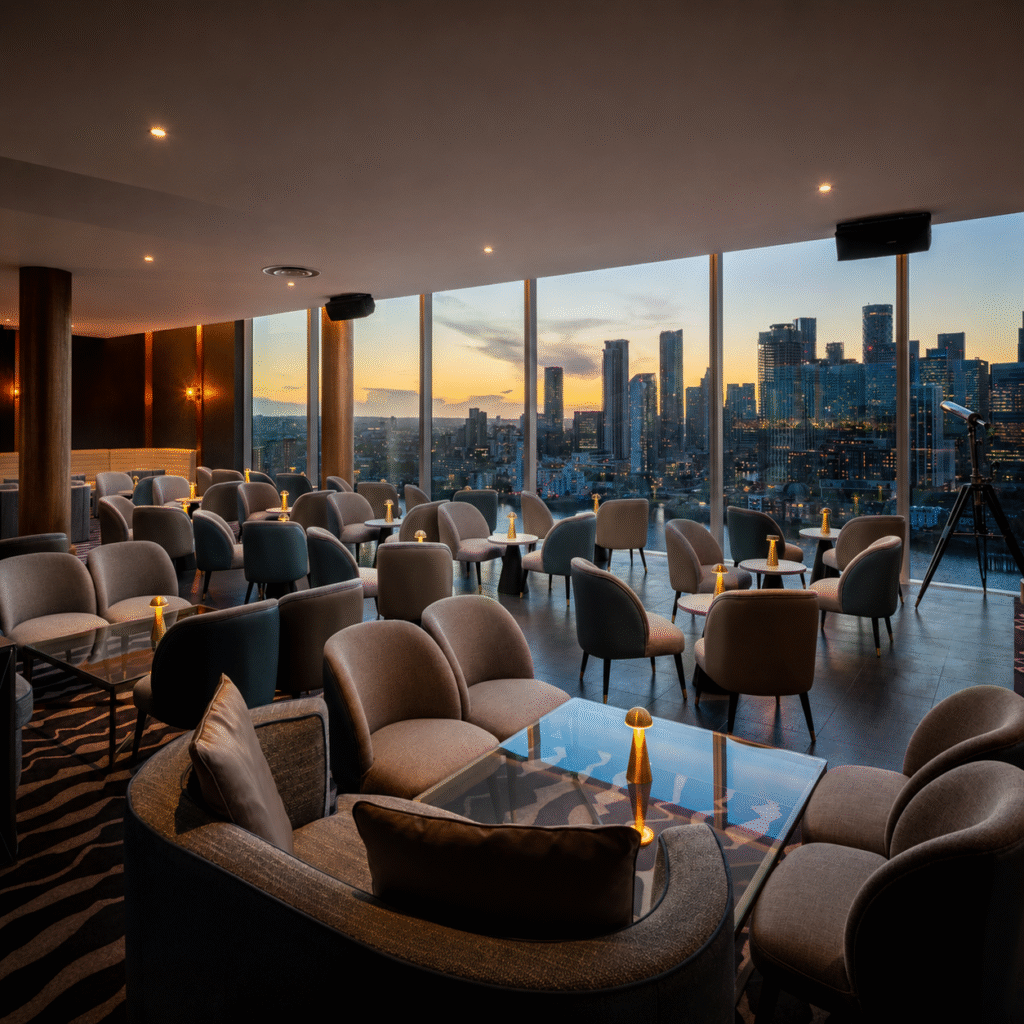 Upscale lounge with plush seating, glass tables, and warm lighting, overlooking a sunset cityscape through floor-to-ceiling windows.