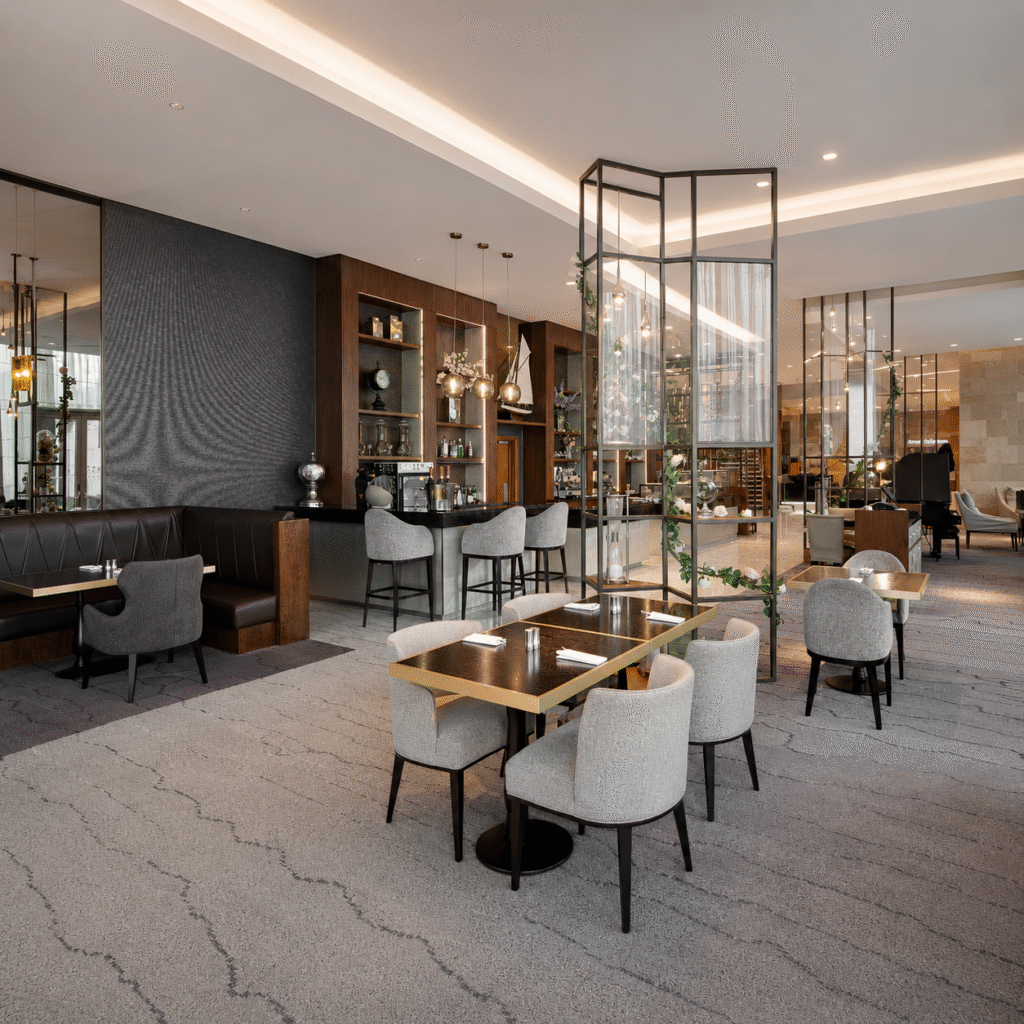 Contemporary restaurant interior with a long dark bar, gray upholstered chairs, and warm pendant lighting.