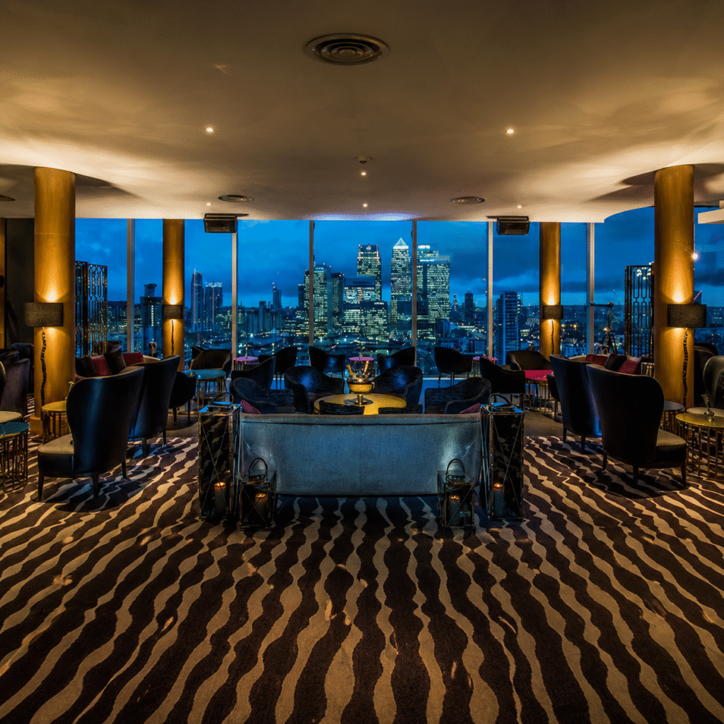 Luxurious lounge with blue velvet seating and floor-to-ceiling windows overlooking a illuminated city skyline at night.