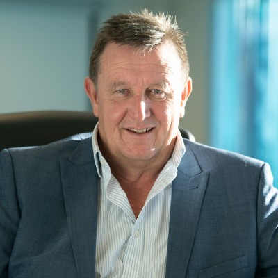 Portrait of a middle-aged man in a blue blazer and light striped shirt, smiling in an office setting.