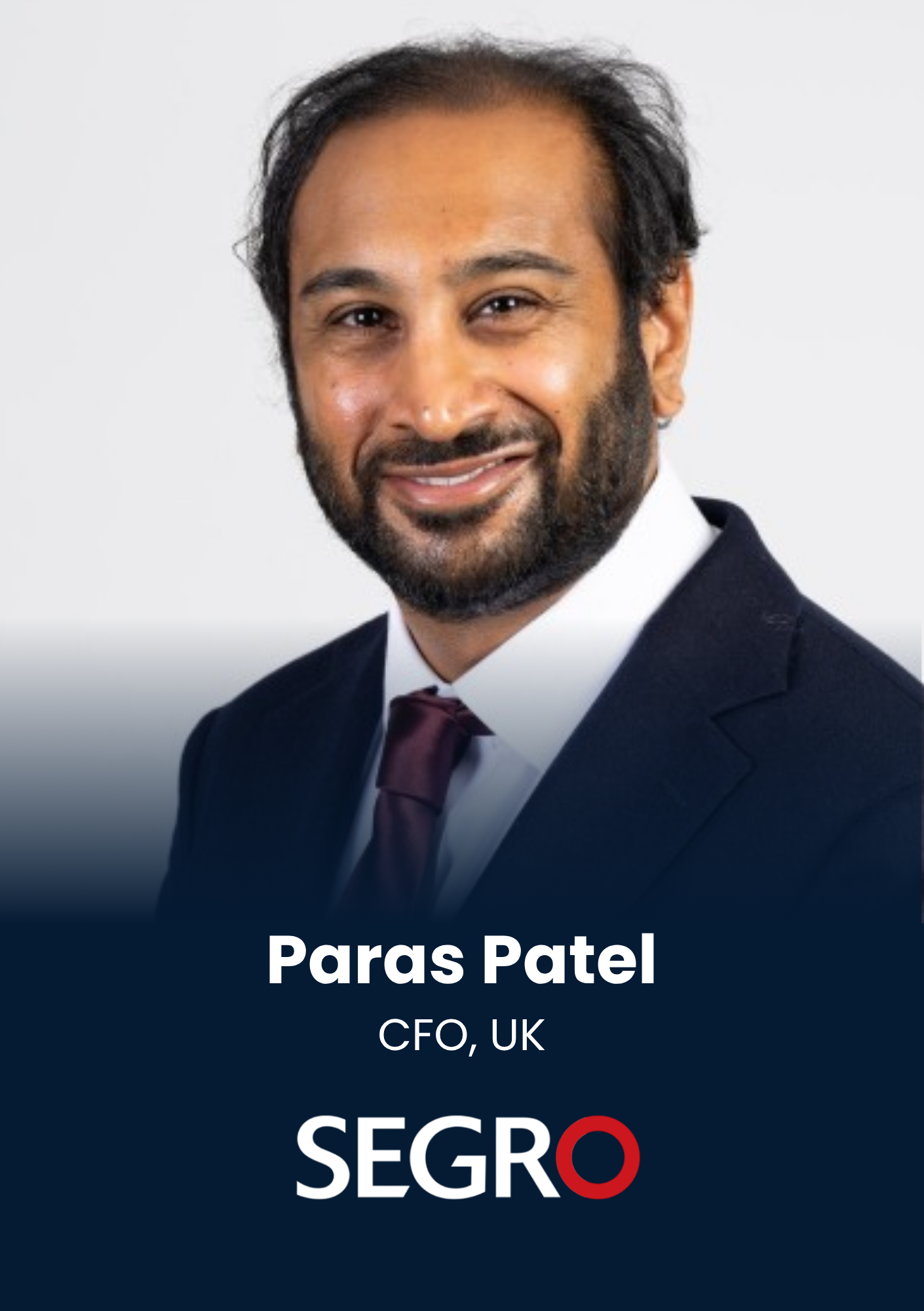 Portrait of Paras Patel, CEO, UK, smiling in a navy suit with a white shirt and burgundy tie, SEGRO branding visible below