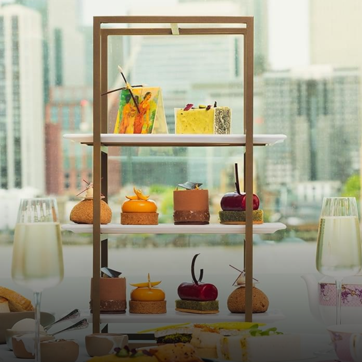 Tiered dessert stand with assorted pastries and small cakes, set against a city skyline.