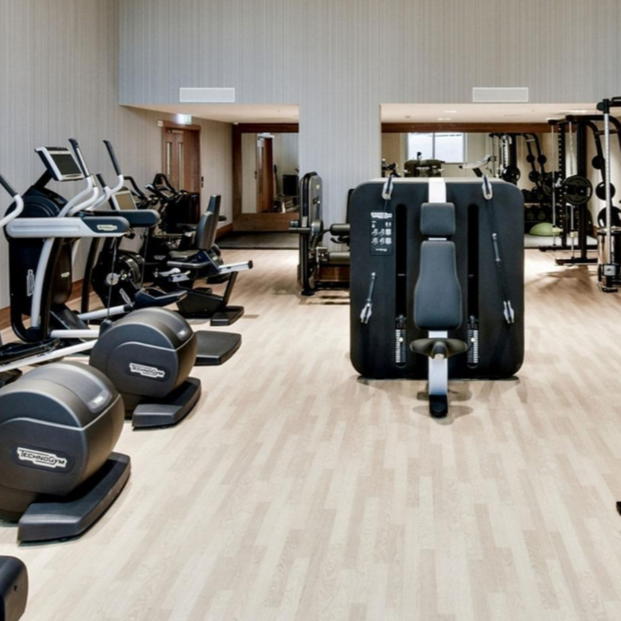 Wide view of a modern gym with treadmills and ellipticals on the left and a large multi-press strength machine in the foreground.