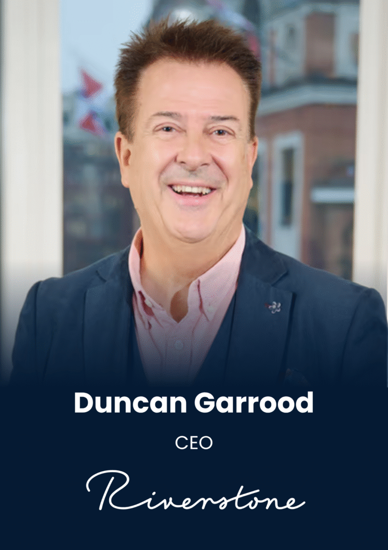 Portrait of Duncan Garrood, CEO, smiling in a navy blazer against a blurred office background.