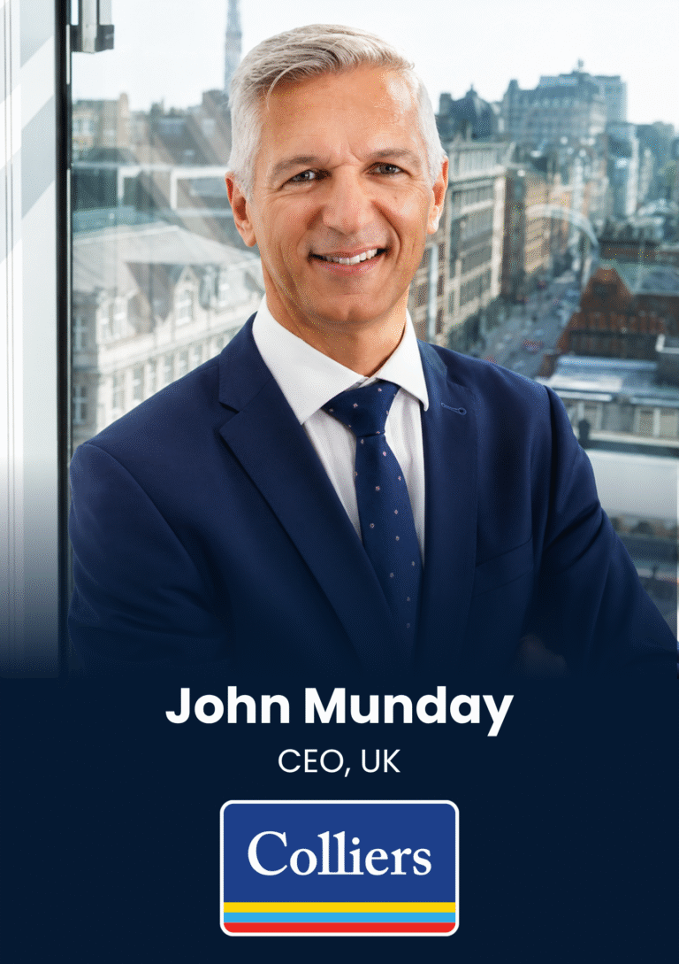 Portrait of John Munday, CEO, UK, smiling in a navy suit with a city skyline behind him.