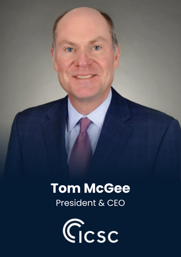 Tom McGee, President & CEO, head-and-shoulders portrait in a navy suit and pink tie, smiling against a gray backdrop