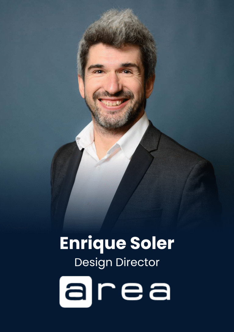 Portrait of Enrique Soler, Design Director, smiling in a dark suit against a blue backdrop.