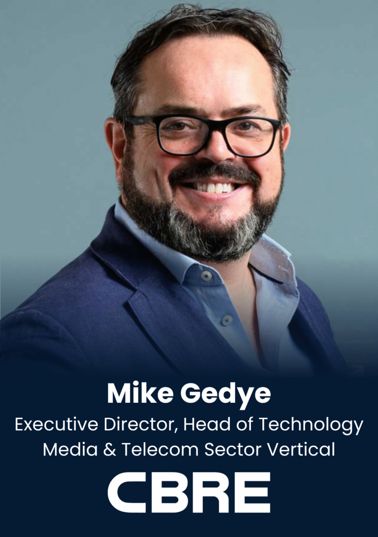 Portrait of Mike Gedye, CBRE executive, smiling and wearing a blue blazer and light blue shirt against a muted blue background.